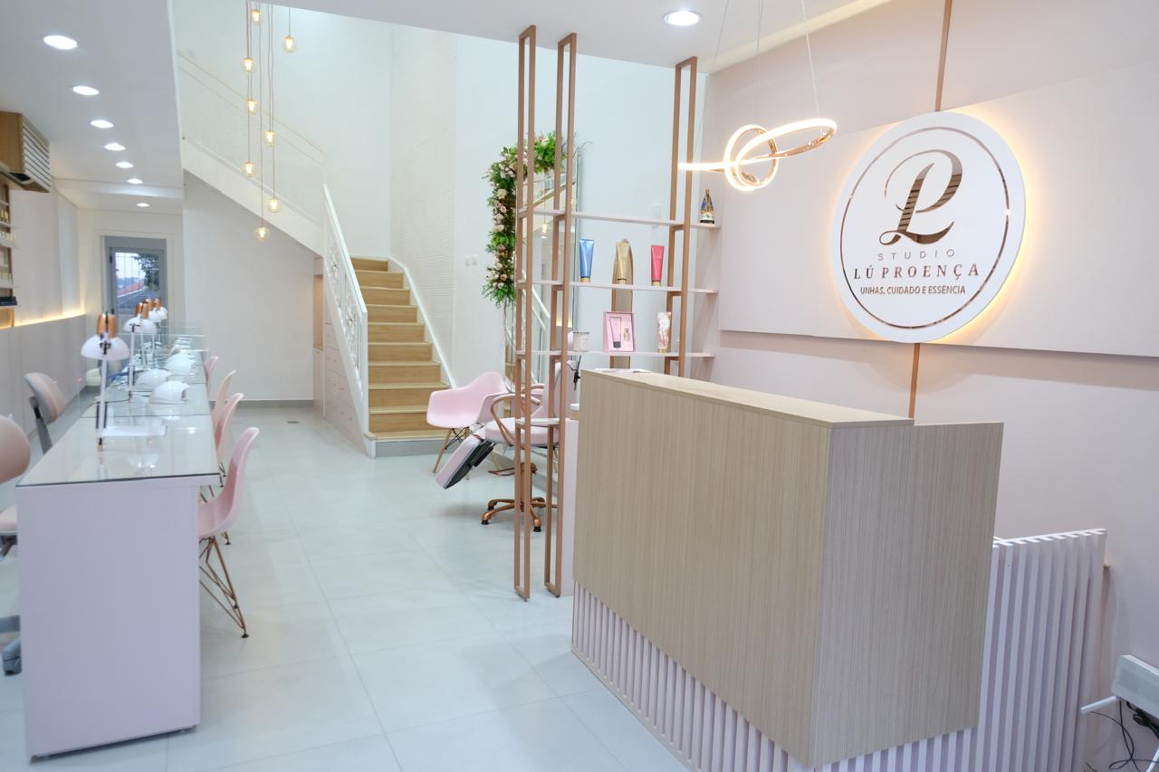 Recepção do Studio Lu Proença, com escada, letreiro iluminado e balcão de atendimento